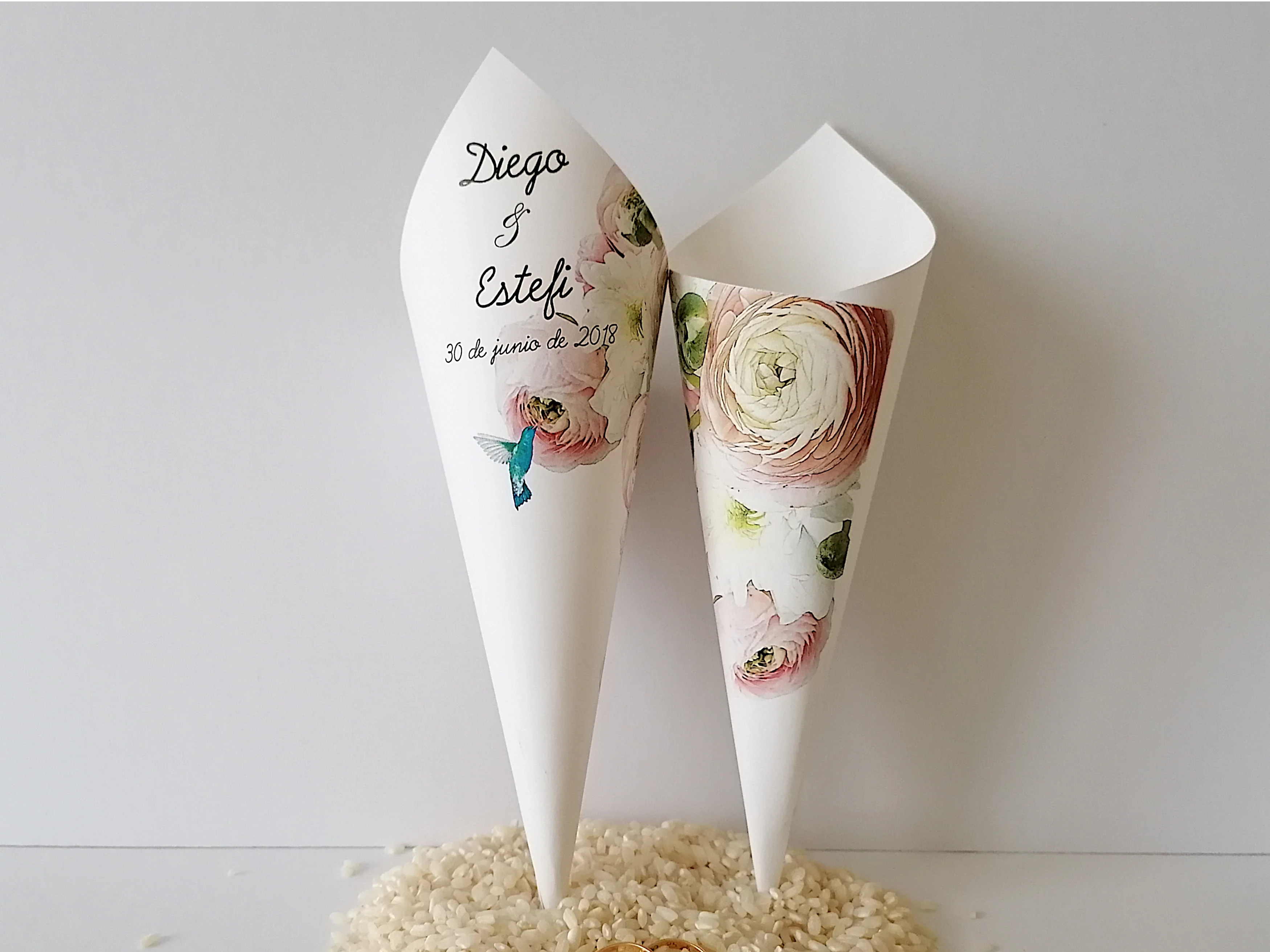 En esta imagen podemos ve Cono o cucurucho de cartulina de 180gr decorado con un diseño floral de ranúnculos y un colibrí. Están pensados para que los invitados a vuestra boda puedan portar con facilidad el arroz, confeti o pétalos para llenar de color vuestra salida del templo ya como matrimonio.