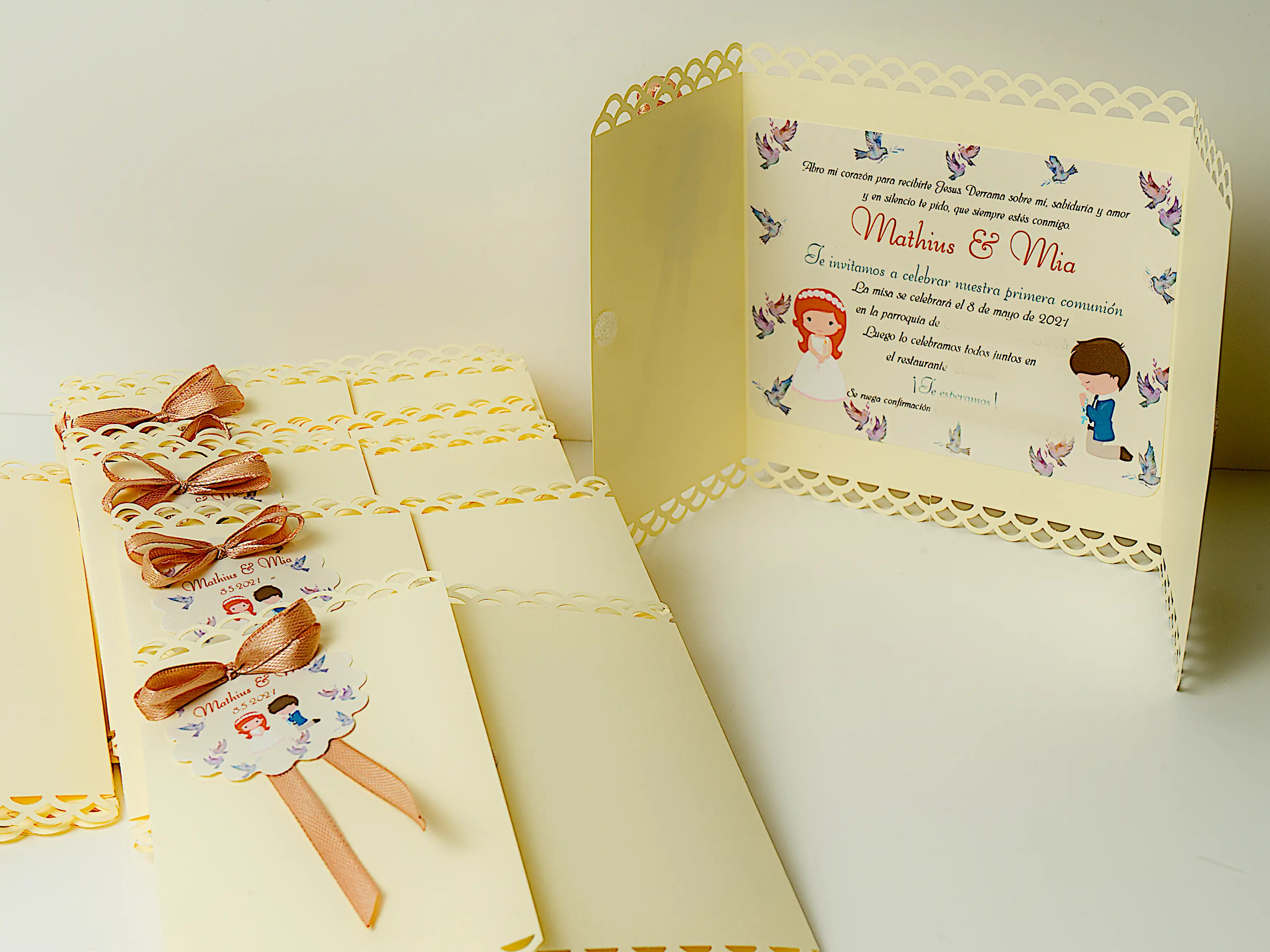 Invitación para comunión mod. Silvia cartulina de 180gm con los bordes troquelados, cierra con un pequeño botón de velcro. En el exterior tiene como adorno un lazo doble que sujeta una etiqueta redonda e ilustrada. En su interior se encuentra una tarjeta con los datos del evento e ilustrada con motivos de comunión.